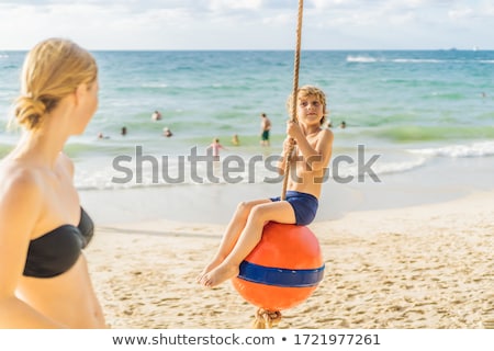 Foto d'archivio: A Boy On A Swing On The Beach Mom And Son Spend Time On The Bea