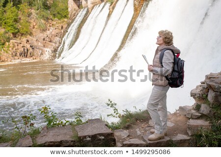 Stock foto: Mature Female Hiker With Backpack And Map Guide Standing By Waterfalls