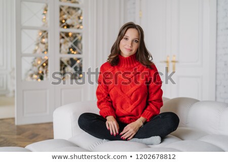 Foto stock: Photo Of Calm Carefree Girl Wears Warm Doemstic Clothes Poses On White Couch Looks Directly At Cam