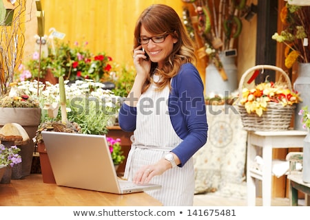 [[stock_photo]]: Smiling Woman Florist Holding Vase With Flowers In The Shop