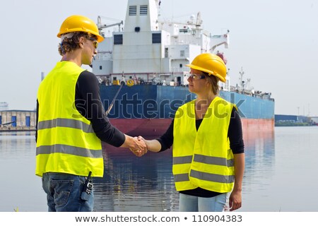 [[stock_photo]]: Female Docker Shakes Hands With A Male Colleague In Front Of A Large Industrial Cargo Ship
