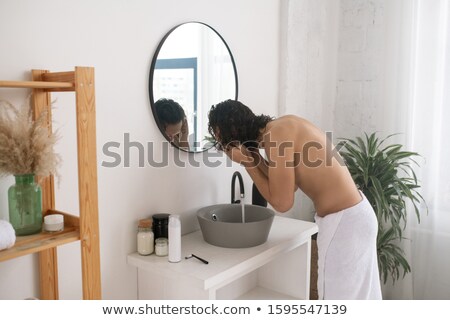 Stock photo: Young Topless Man Bending Over Bowl In Front Of Mirror While Washing His Face