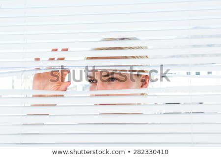 Foto stock: Curious Blonde Woman Looking Through Venetian Blind