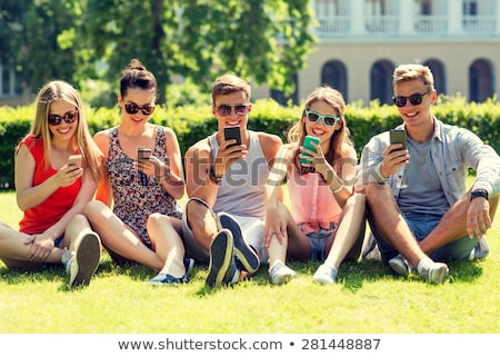 Foto stock: Smiling Friends With Smartphones Sitting On Grass