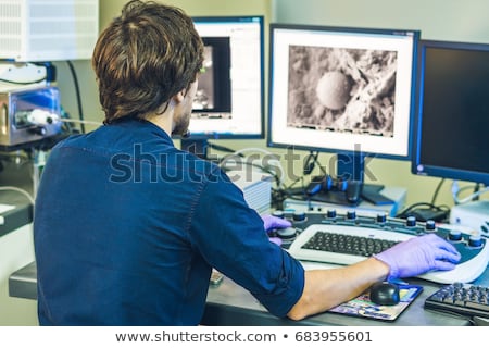 Foto stock: Scientist Works At A Electron Microscope Control Pannel With Two Monitors In Front Of Him