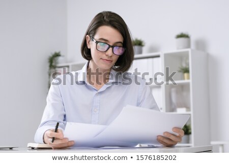Stock photo: Young Serious Female Accountant In Eyeglasses And Formalwear Reading Papers