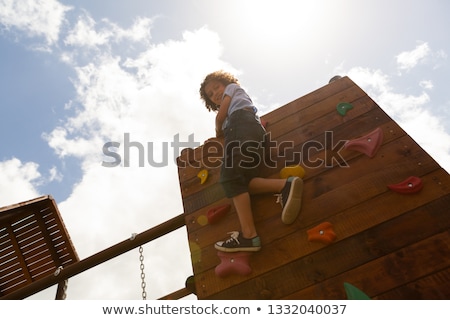 ストックフォト: Low Angle View Of A Mixed Race Schoolgirl Climbing A Wall In The School Playground On A Sunny Day