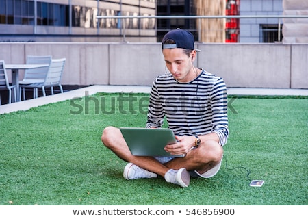 Stock photo: Stylish Young Man In Shorts And Cap Sitting With A Laptop In Open Window
