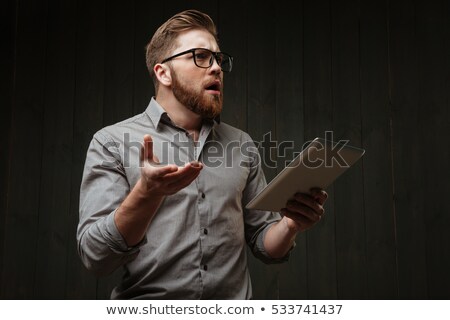 Stock photo: Surprised Bearded Man In Eyeglasses Holding Tablet Computer And Gesturing
