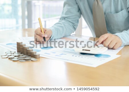 Stockfoto: Businessman Using Calculator With Stacked Coins Arranged At Offi