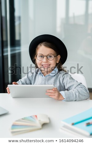 [[stock_photo]]: Smiling Schoolgirl Looking At You While Sitting By Desk And Drawing With Crayons