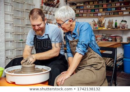 Stok fotoğraf: Senior Woman Spinning Clay On A Wheel With Teacher At Pottery Cl