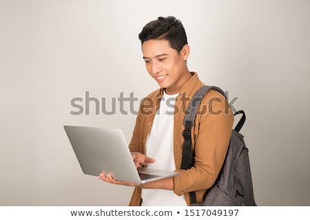 Stok fotoğraf: Smiling Asian Man Student With Backpack Using Laptop