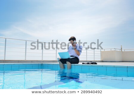 Stockfoto: Young Man Dressed In Bathrobe Sitting On The Edge Of A Swimming Pool And Drinking Coffee