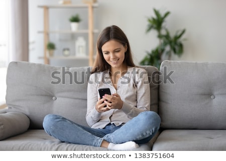 Stok fotoğraf: Young Casual Woman With Smartphone Sitting On Couch In Restaurant And Messaging