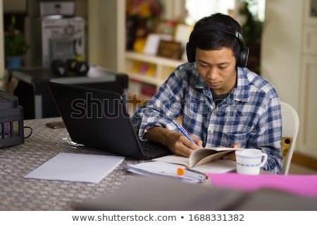 [[stock_photo]]: Young Serious Asian Man Writing In Notebook And Using Laptop