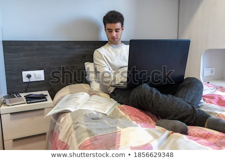 Foto stock: Young Man Is Working On A Laptop In His Bed On A Background Of A Panoramic Window Overlooking The Sk