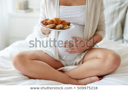 Zdjęcia stock: Happy Pregnant Woman Eating Cookie In Bed At Home
