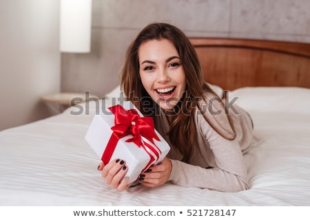 Stockfoto: Smiling Happy Woman With Gift Box Lying In Bed And Looking At Camera