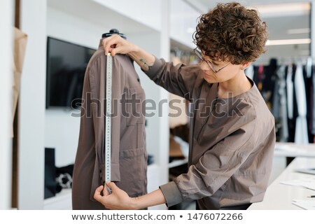 Stock fotó: Young Brunette Curly Woman Measuring Sleeve Length Of Jacket On Mannequin