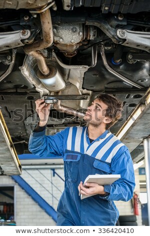 [[stock_photo]]: Mechanic Examining Exhaust System Of Car With Flashlight