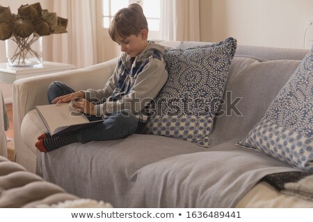 Foto stock: Side View Of Young Boy Sitting In Stylishly Decorated Living Room Reading A Story Book