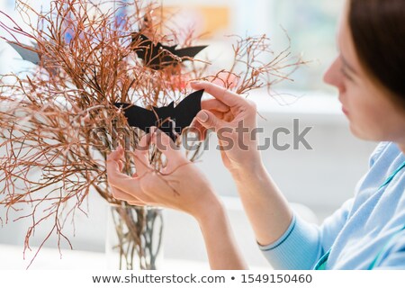 Foto d'archivio: Hands Of Young Female Holding Black Handmade Bat And Hanging It On Branches