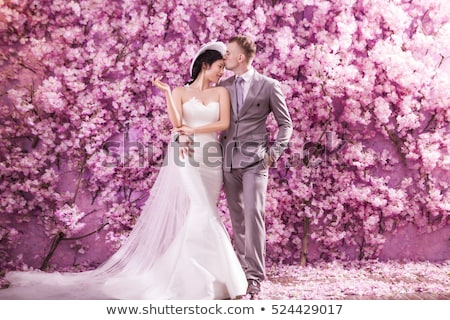 Stock foto: Romantic Bridegroom Kissing Bride On Forehead While Standing Against Wall Covered With Pink Flowers