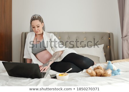 Stock photo: Cheerful Pregnant Young Woman Lying And Using Laptop On Bed