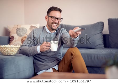 Stockfoto: Portrait Of Young Man Sitting On The Sofa While Watching Tv At H