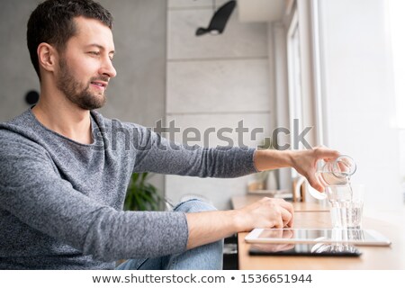 Stockfoto: Casual Man Sitting By Window In Cafe And Pouring Water From Bottle Into Glass