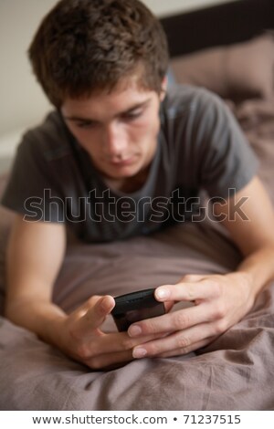 ストックフォト: Unhappy Teenage Boy Lying In Bedroom With Mobile Phone