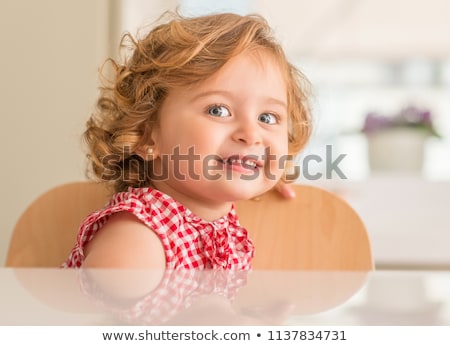 Stockfoto: Adorable Toddler With Charming Blue Eyes And Blonde Hair Sits On Floor Against Home Interior Plays