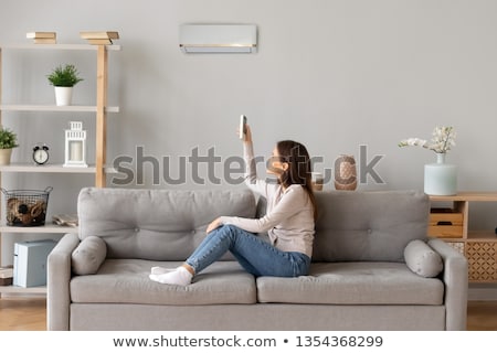 Stok fotoğraf: Woman Operating Air Conditioner With Remote Control