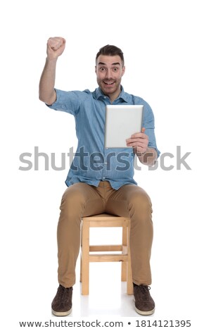 Foto stock: Seated Man Holding Tablet Celebrates Success With Hands Up