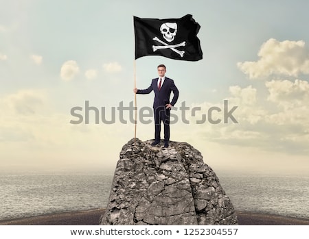 Foto d'archivio: Businessman On The Top Of A Rock Holding Pirate Flag