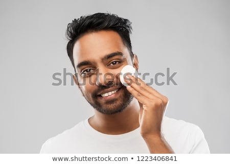 Foto stock: Smiling Indian Man Cleaning Face With Cotton Pad