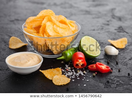 Foto stock: Glass Bowl Plate With Potato Crisps Chips With Paprika Flavour On Black Stone Table Background Red