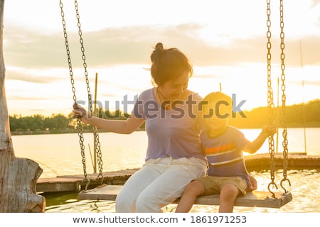 Foto stock: Happy Boy Sit On Swing At The Sea Shore On Sunset