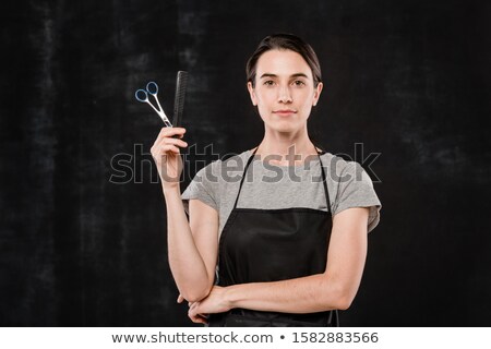 Stock foto: Young Serious Hairdresser In Workwear Holding Hairbrush And Scissors
