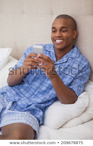 ストックフォト: Handsome Man Sitting On Bed Sending A Text Message