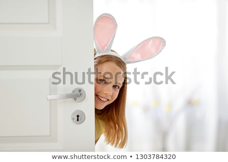 Foto stock: Happy Girl With Easter Bunny Ears Peeking Out Door