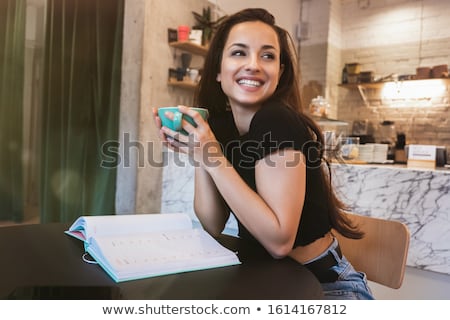 Foto d'archivio: Beautiful Woman Looking To A Coffee Bean In Her Hand Sitting On A Table With Cappuccino Coffee