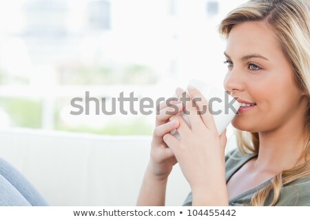 Zdjęcia stock: A Woman Sitting Across The Couch With Raised Knees And Cup Held To Her Lips All While Smiling