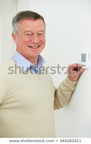 [[stock_photo]]: Smiling Senior Man Adjusting Central Heating Thermostat