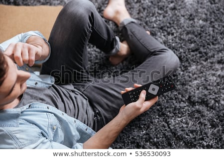 Foto stock: Man Talking On Phone While Choosing Tv Channels With Remote