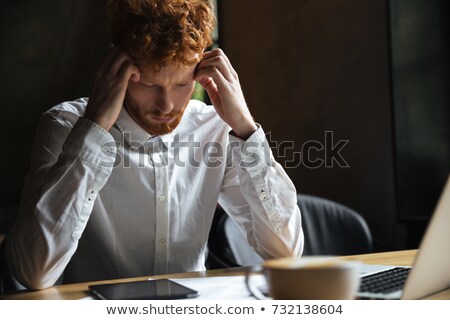 Stockfoto: Photo Of Tired Readhead Curly Bearded Man Sitting On Wooden Tab