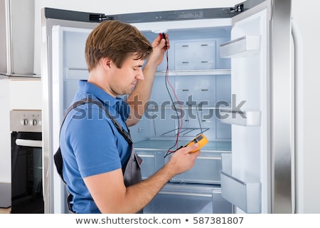 Stock foto: Serviceman In Overall Working On Fridge