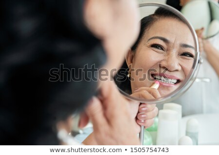 Stok fotoğraf: Smiling Senior Woman Applying Lipstick To Her Lips