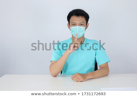 Сток-фото: Young Asian Man Withwearing A Surgical Mask Brings His Hand To His Nose As A Sign Of Silence Isol
